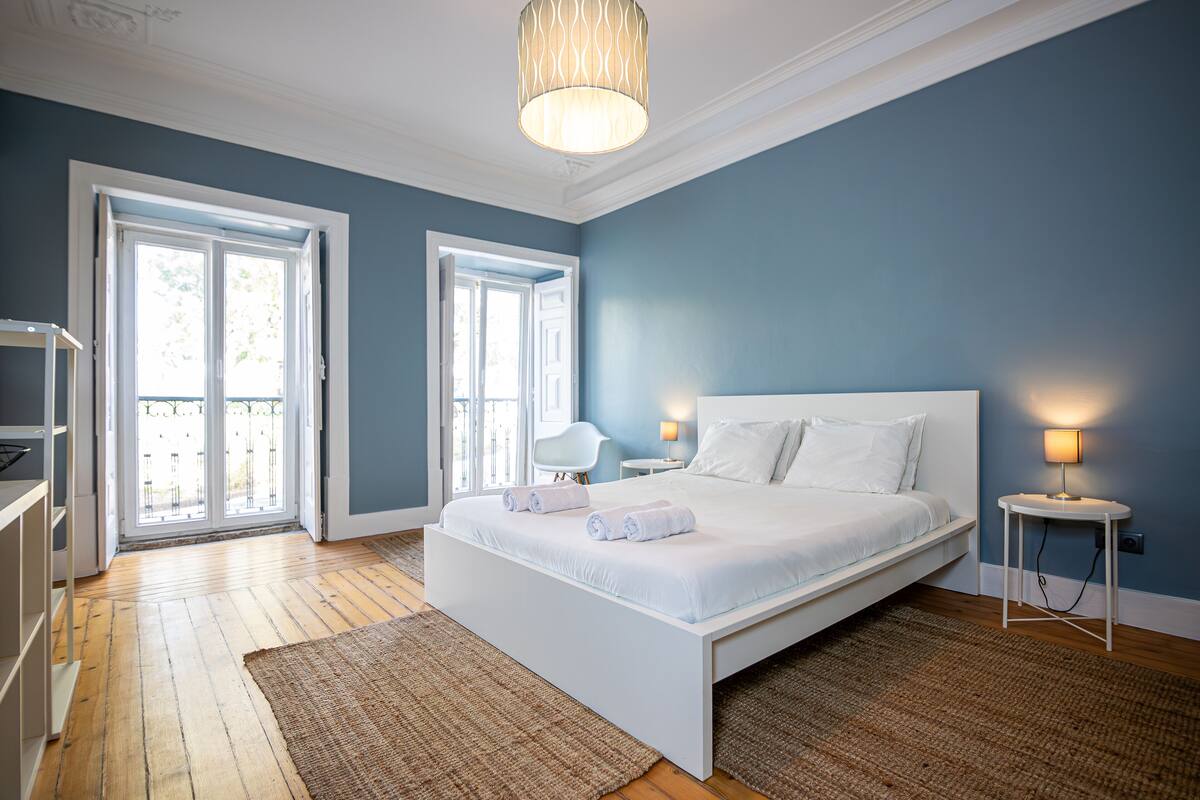A bedroom with a large bed, a bedside table with a lamp, and a view through a door to an outdoor balcony.