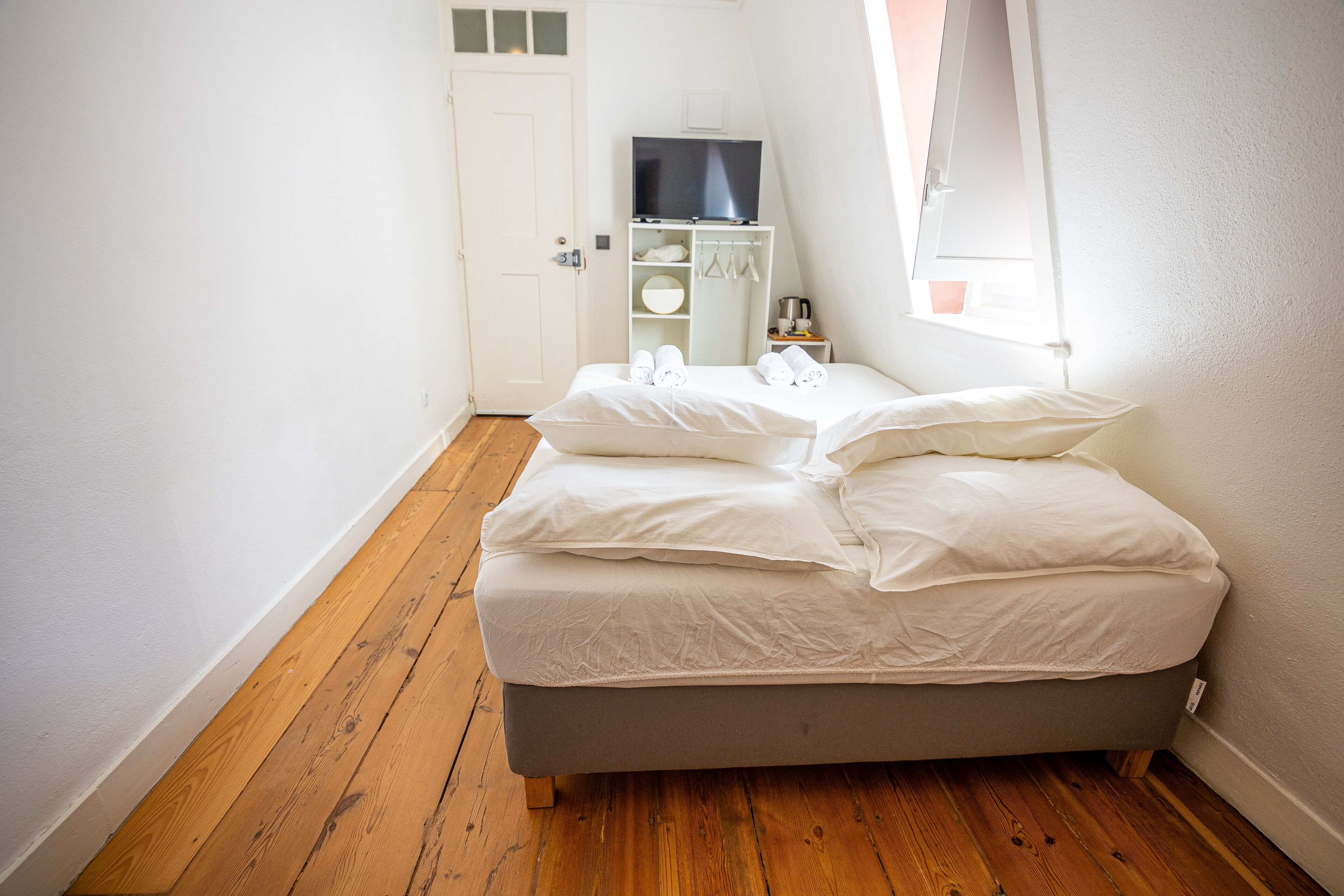 Un dormitorio con una cama, un televisor sobre un mueble y una puerta.