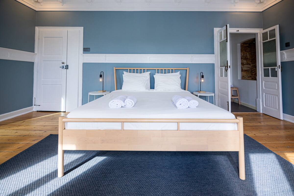 A bedroom with a wooden bed, white bedding, and a blue wall.