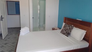 A neatly made bed with white linens and a wooden headboard, a small bedside table with a lamp, and a blue wall. - Hotel Principal (Tarrafal)