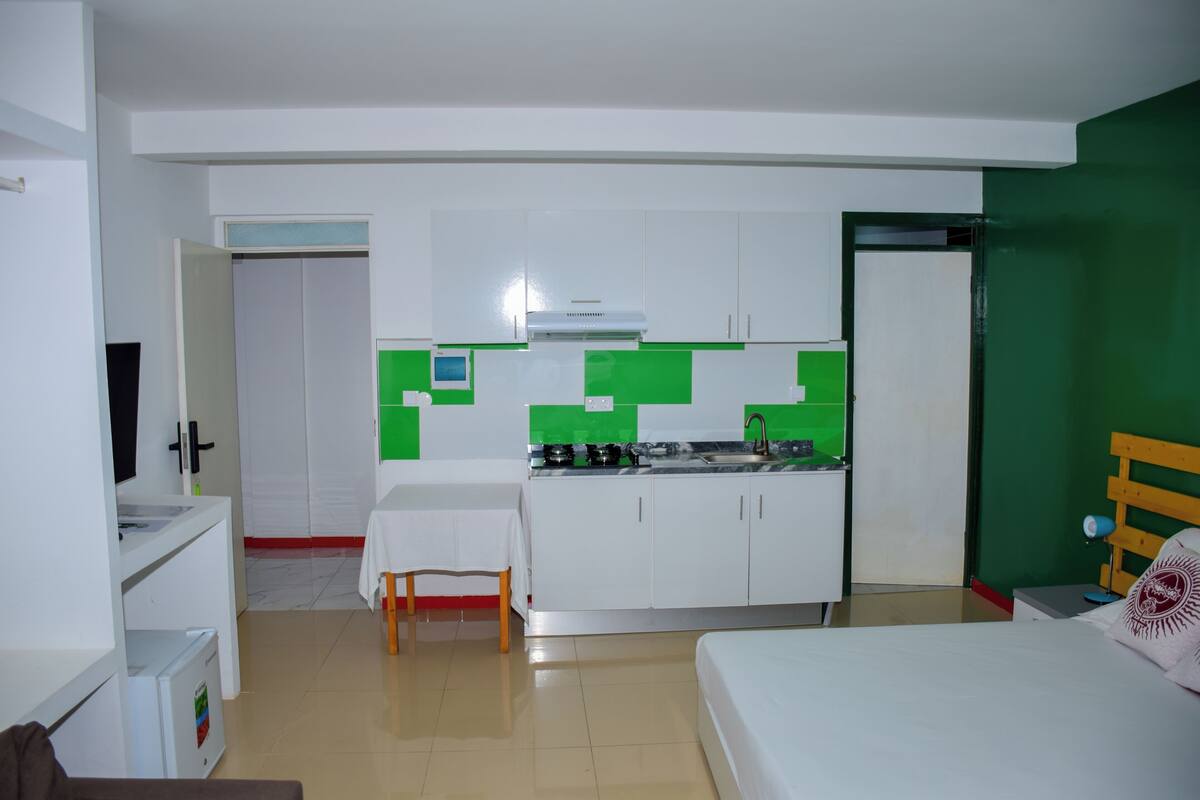 Una habitación pequeña con kitchenette, cama y una mesita.