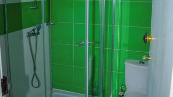 Un baño con ducha de vidrio, inodoro y paredes con azulejos verdes.