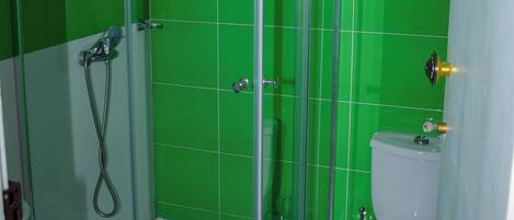 Un baño con ducha de vidrio, inodoro y paredes con azulejos verdes.
