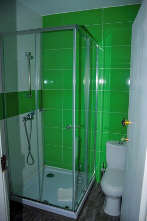 A bathroom with a glass-enclosed shower, a toilet, and green tiled walls. - Hotel Principal (Tarrafal)