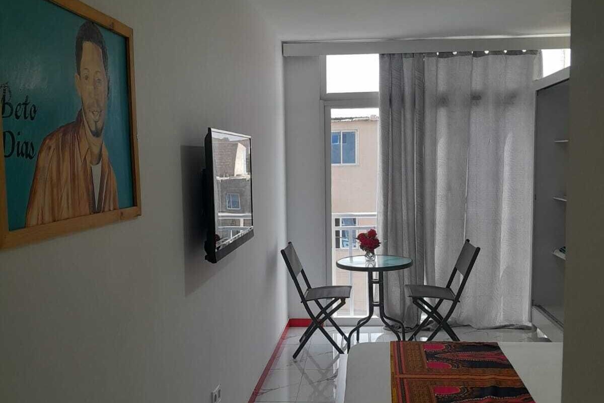 A hotel room with a bed, a painting, a small table with chairs, and a view through a window.