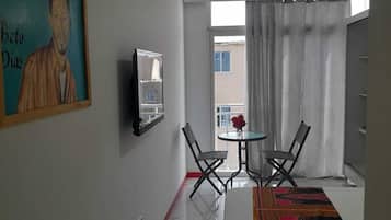 A hotel room with a bed, a painting, a small table with chairs, and a view through a window.