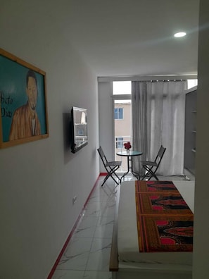 A hotel room with a bed, a painting, a small table with chairs, and a view through a window. - Hotel Principal (Tarrafal)