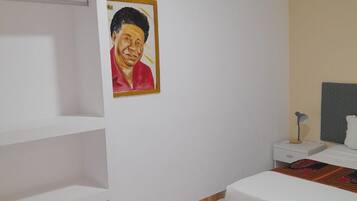 Un dormitorio con cama, mesita de noche, lámpara, estante y un cuadro en la pared.