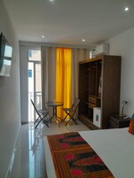 Habitación de hotel con una cama, armario, una mesita con sillas y una ventana con cortinas.