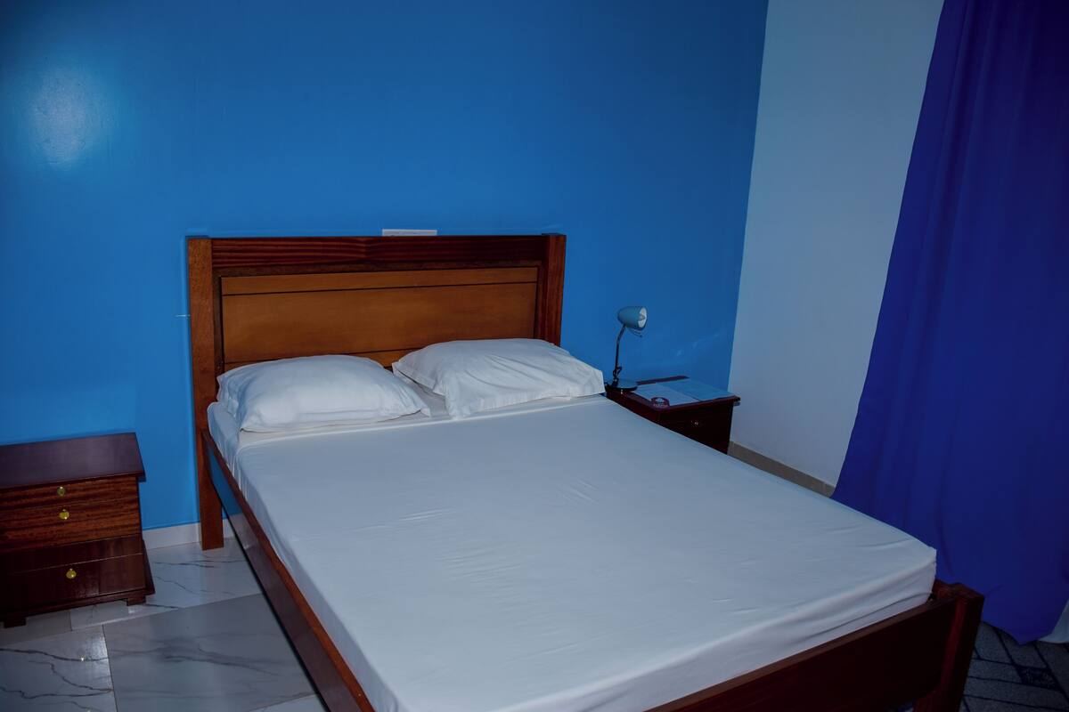 Una cama bien tendida con sábanas blancas en una habitación con paredes azules y un cabecero de madera.