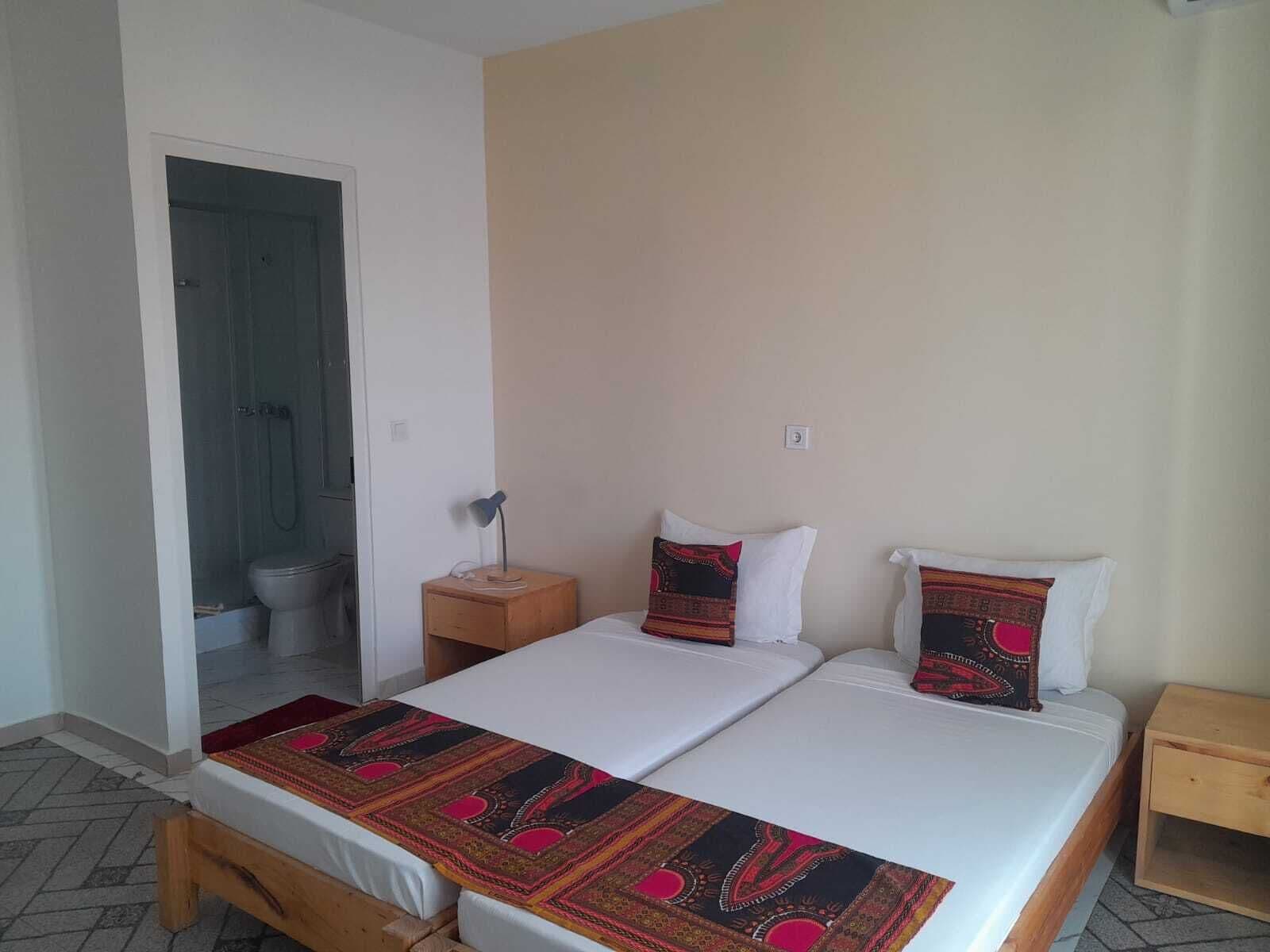 A double bed with a patterned bedspread, a bedside table with a lamp, and a wooden nightstand.