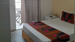Une chambre d’hôtel avec un lit, une table de chevet, une commode, un tableau au mur et une vue par la fenêtre, qui est dotée de rideaux.
