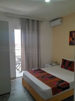 Habitación de hotel con cama, mesita de noche, cuadro en la pared y vistas a través de una ventana con cortinas.