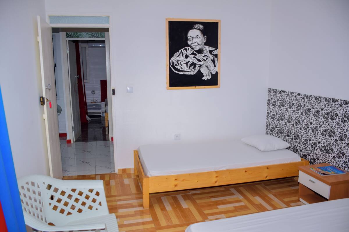 Un dormitorio con una cama de madera, una silla blanca, una mesita de noche pequeña y una pared con papel tapiz estampado.