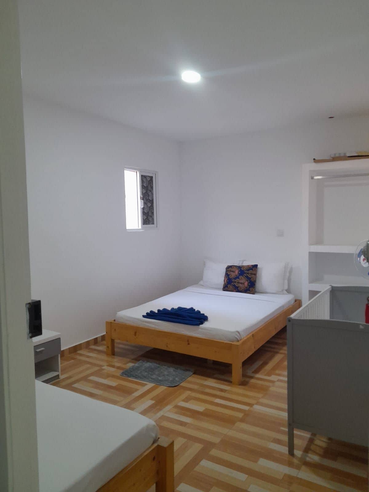 Habitación individual con cama de madera, mesita de noche pequeña, una silla, escritorio y armario.