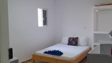Habitación individual con cama de madera, mesita de noche pequeña, una silla, escritorio y armario.