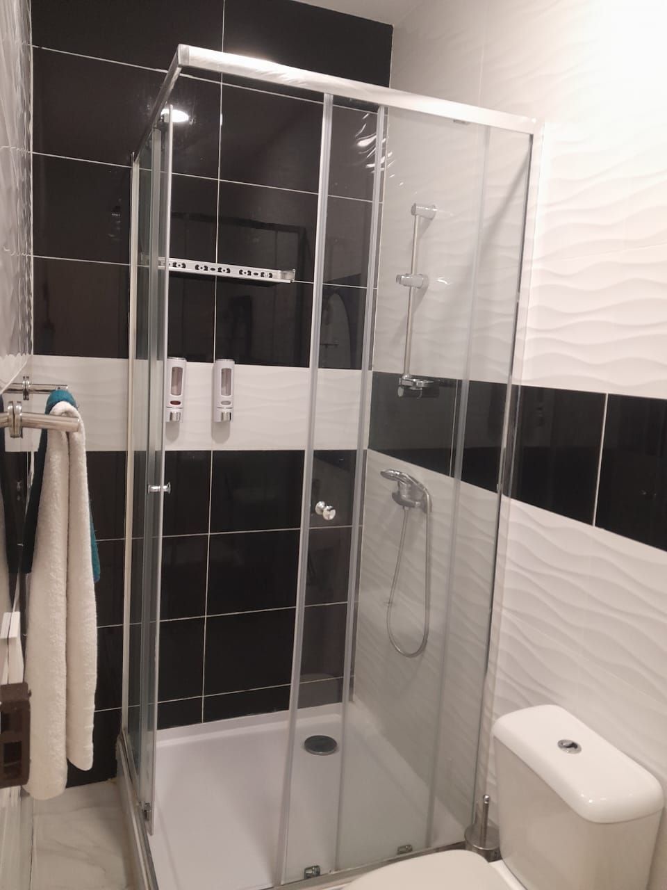 A glass-enclosed shower stall with a white toilet and a towel rack with towels.