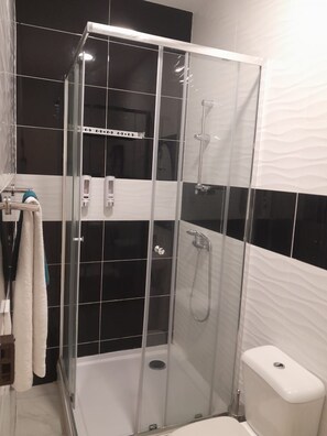 Un vestuario con ducha de vidrio, inodoro blanco y toallero con toallas.