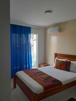 Un dormitorio con cama, una mesita de noche, una ventana con cortinas azules y un equipo de aire acondicionado en la pared.