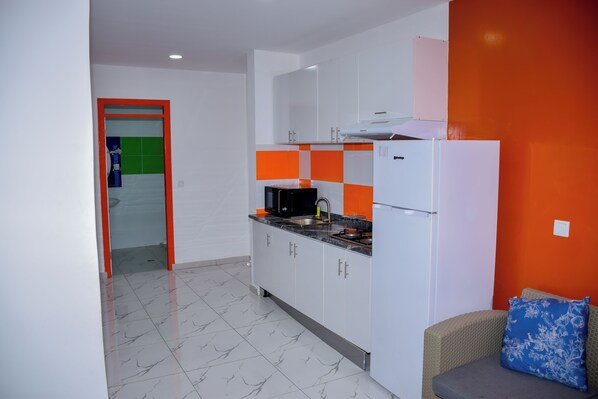 A modern kitchen with white cabinets, a black countertop, and a red and white backsplash. - Hotel Principal (Tarrafal)
