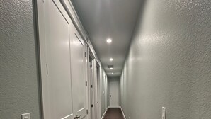 Un pasillo largo y estrecho con puertas blancas a un lado y suelo de madera.