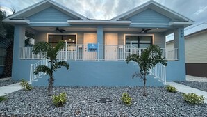 Un edificio residencial de dos plantas con fachada azul, un balcón con barandilla blanca y un letrero que dice 'For Rent'.