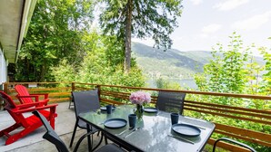 Mesa para cuatro personas con un florero, sillas Adirondack rojas y vistas a un lago y montañas.