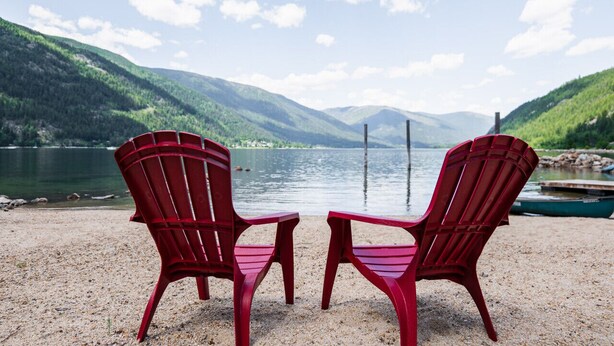 Dos sillas Adirondack rojas mirando un lago con montañas al fondo.