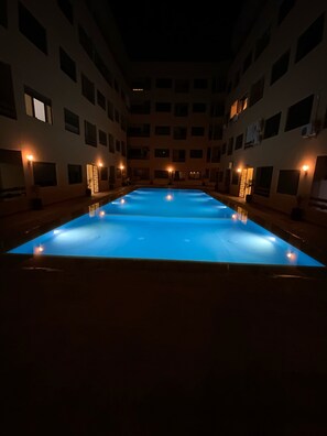 Ein großes Hallenbad mit blauem Boden, umgeben von einem mehrstöckigen Gebäude mit gleichmäßig verteilten Fenstern und Wandleuchten.