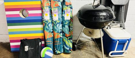 Een kleurrijk gestreept bord, een zwarte tas, een volleybal, een barbecue en een koelbox.