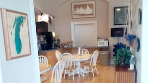 Un comedor con sillas blancas y una mesa de madera, un reloj en la pared y un televisor montado.