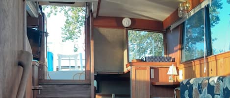 A compact RV interior with a wooden staircase leading to a sleeping area, a small kitchenette, and a dining table.