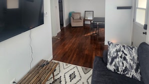A living room with a flat-screen TV, a ceiling fan, a patterned rug, a dark sofa with a patterned pillow, and a dining area with a table and chairs. - tiny house backyard cabin getaway in Detroit (Detroit)