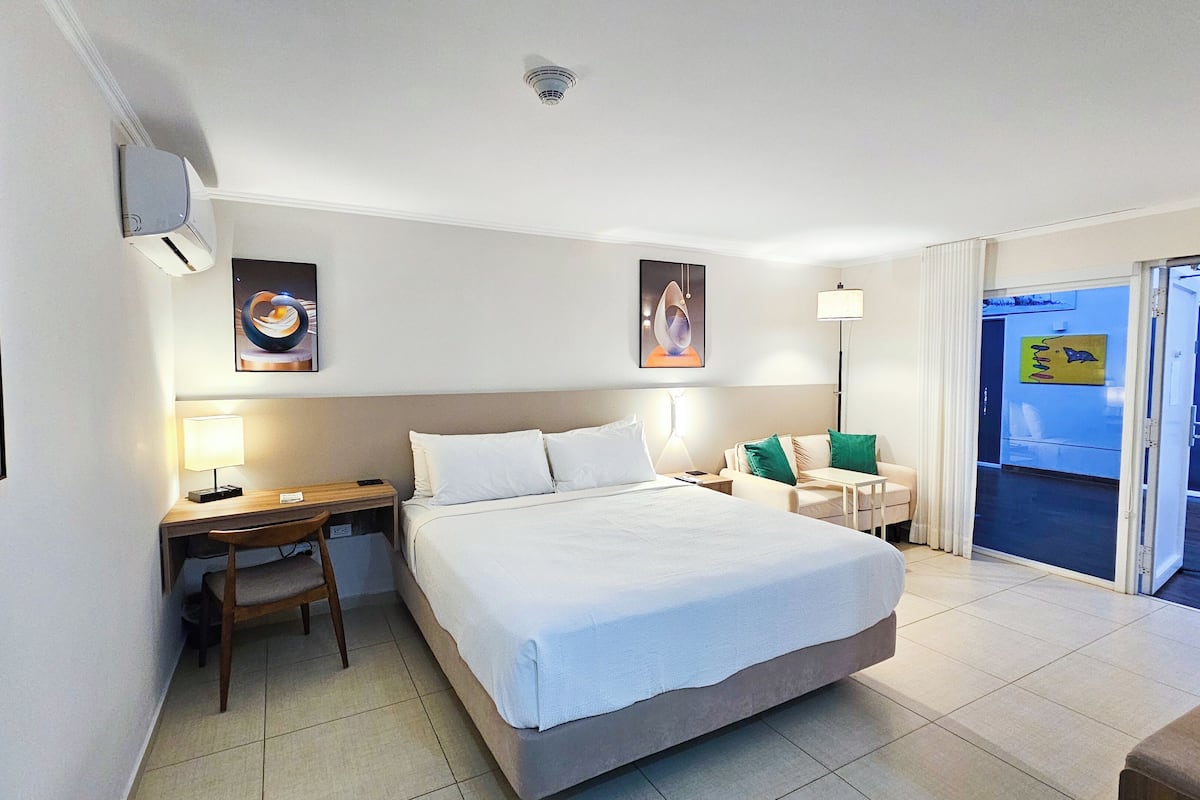 A hotel room with a bed, a desk, a chair, a nightstand, and a door leading to a balcony.