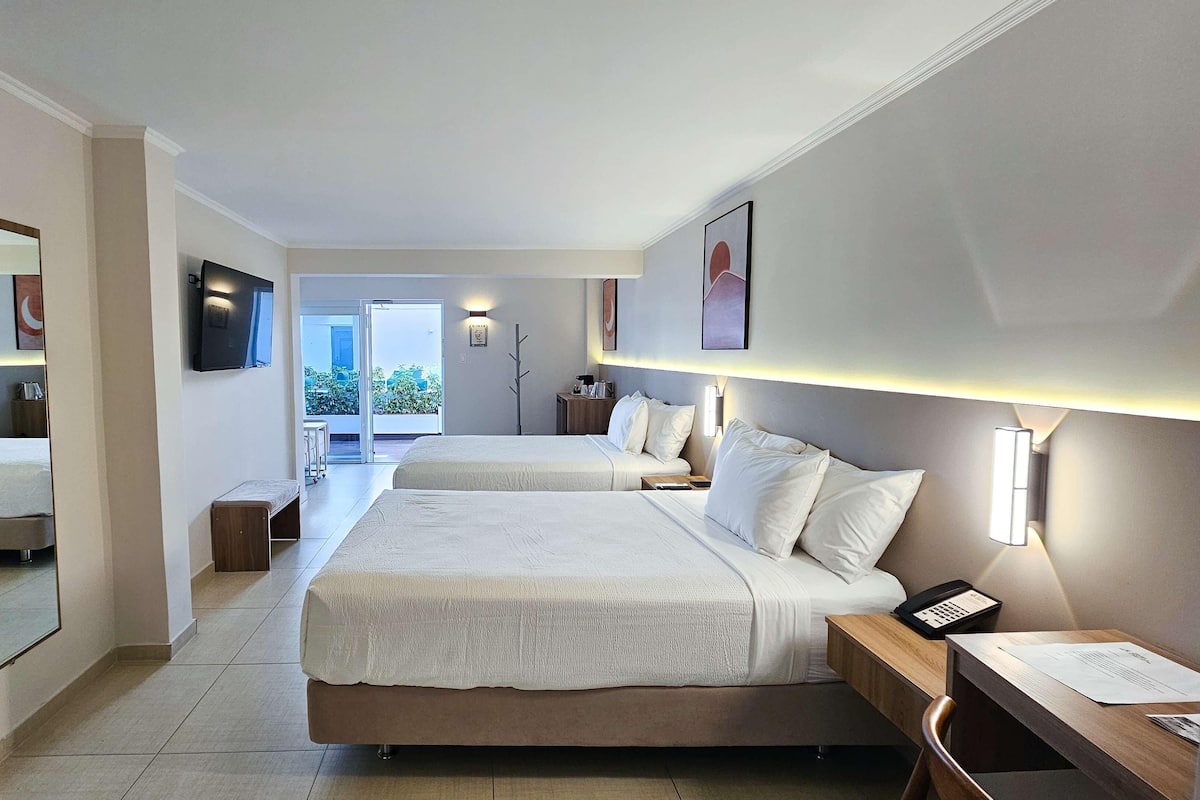 A hotel room with two beds, a desk, a chair, a wardrobe, and a television.