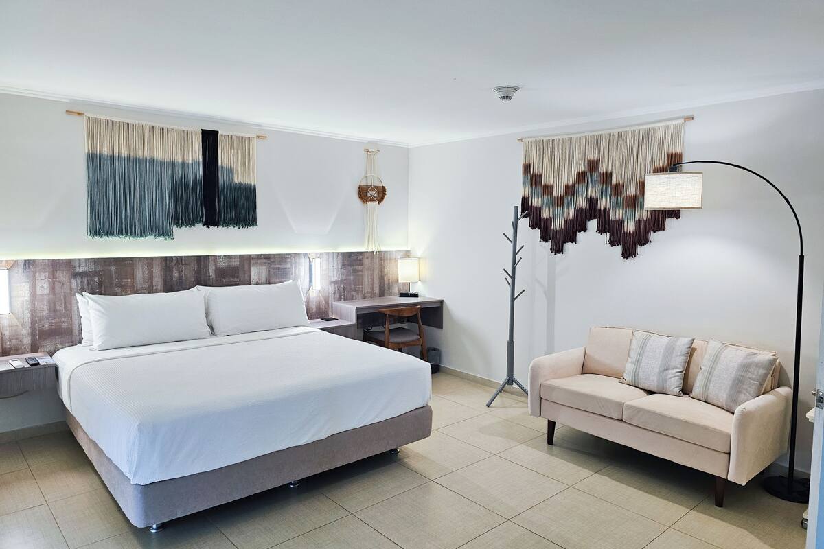 A modern hotel room with a large bed, a sofa, a desk, and a floor lamp.