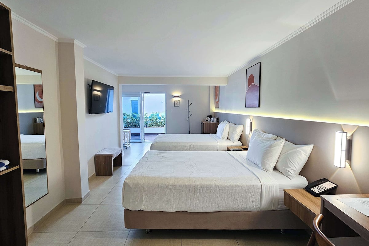 A hotel room with two beds, a desk, a chair, a wardrobe, and a TV.