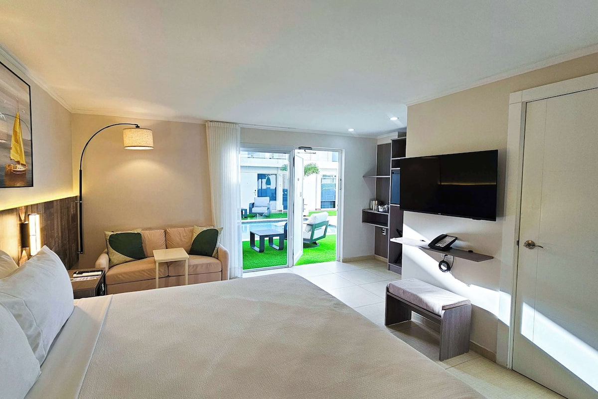 Relax in this spacious room with a large bed, flat-screen TV, and access to an outdoor area with a pool and seating.