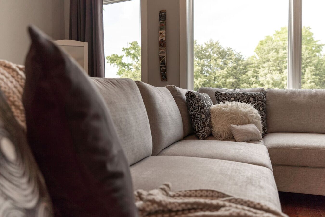 A modern living room with a beige sectional sofa, patterned throw pillows, and a decorative wall piece.