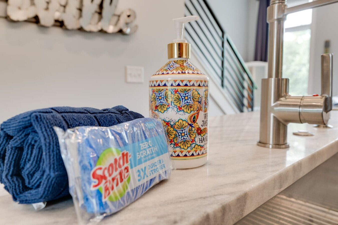 Un meuble de salle de bain avec une serviette bleue, une bouteille de produit nettoyant Scotch-Brite Zero Scrub et un récipient décoratif en céramique.