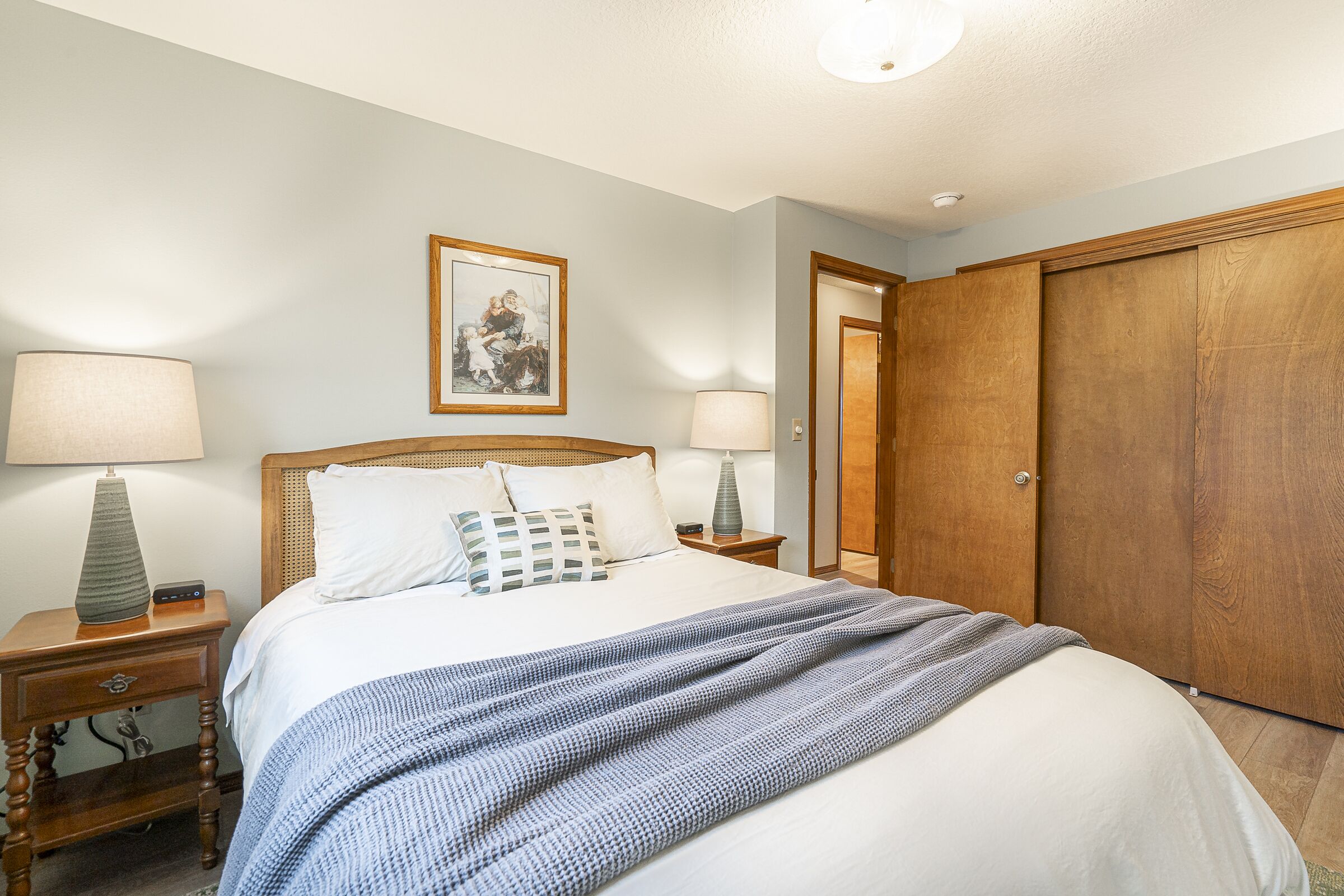 A neatly made bed with a blue and white striped blanket, two bedside lamps, a framed picture on the wall, and a wooden wardrobe.