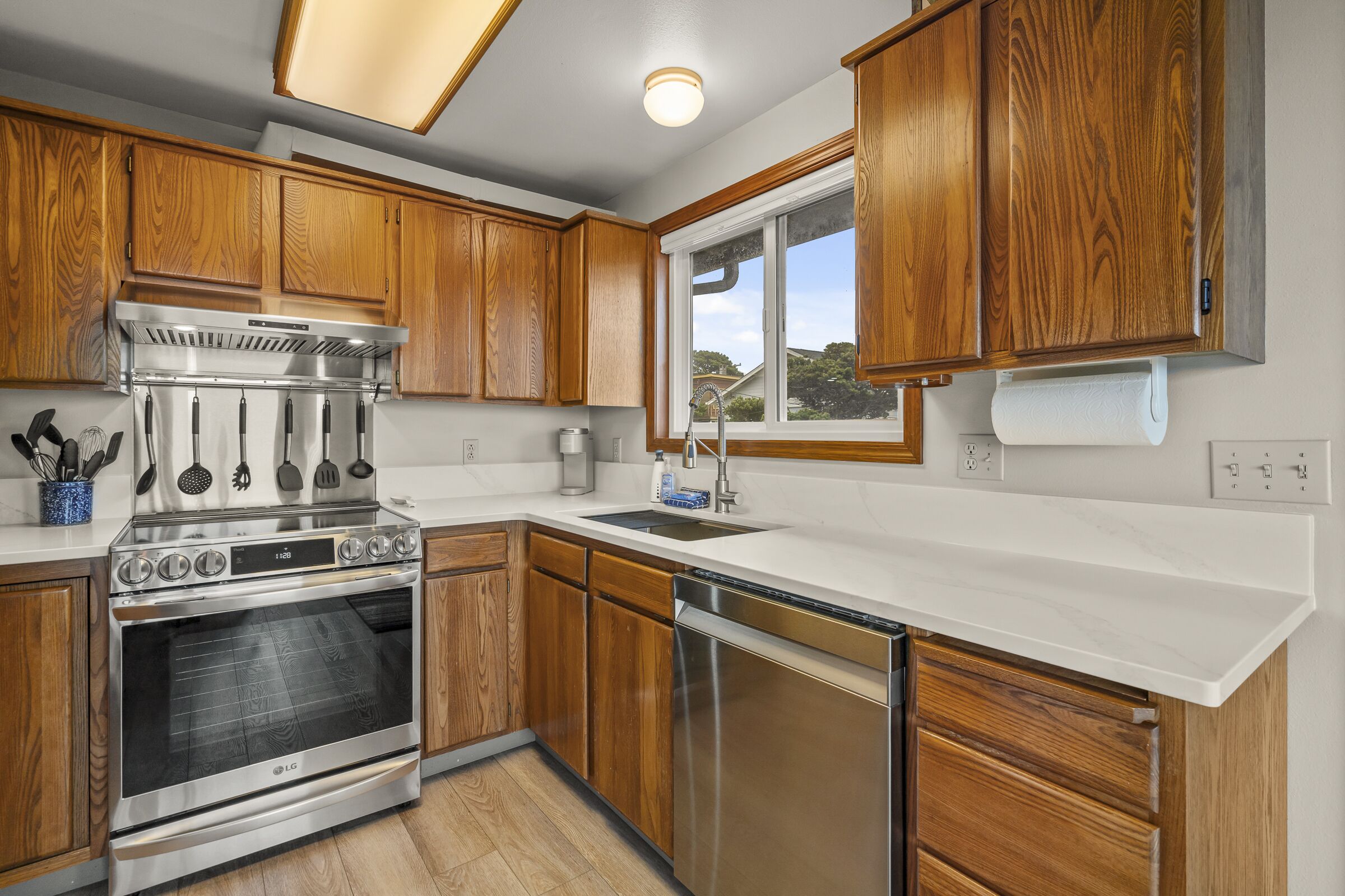 A modern kitchen with wooden cabinets, stainless steel appliances, and a large window providing natural light.