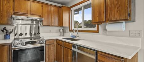 A modern kitchen with wooden cabinets, stainless steel appliances, and a large window providing natural light.
