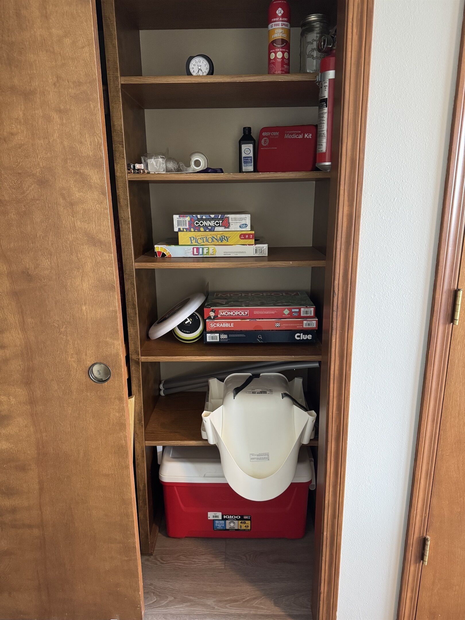 A wooden shelf unit with various items including a clock, fire extinguisher, and board games.