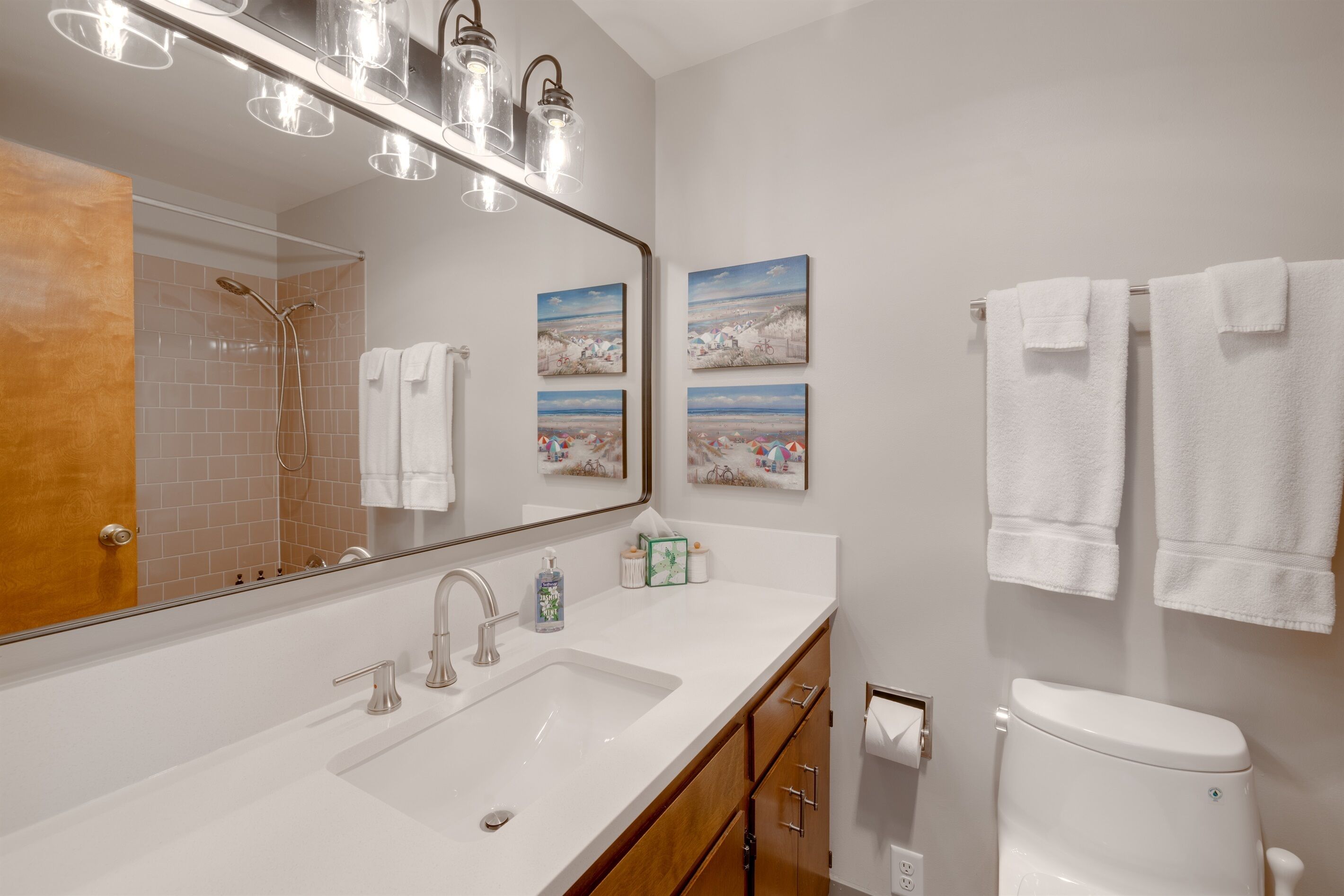 A modern bathroom with a large mirror, a white sink, a shower, and two white towels hanging on the wall.