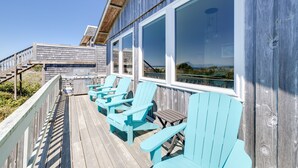 A wooden deck with turquoise Adirondack chairs and a wooden railing. - Luxurious & Cozy Oceanfront Escape Steps from the Sand with Sweeping Ocean Views (Rockaway Beach)