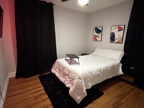 Un dormitorio con cama, una mesita de noche, una lámpara negra y dos cuadros en la pared.