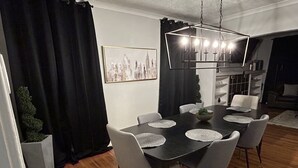 Et spiseområde med et sort bord og grå stole, et bybillede på væggen, samt en moderne lysekrone.