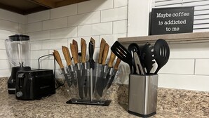 En køkkenbordplade med et knivdisplay, en brødrister og et skilt med teksten "Måske er jeg afhængig af kaffe".