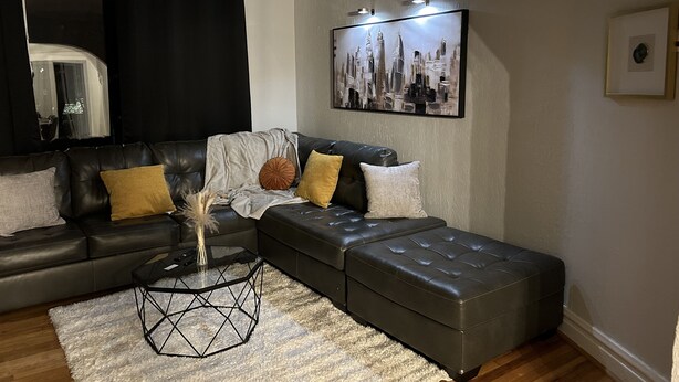 En moderne stue med en hjørnesofa, skammel og et sofabord med geometrisk design.